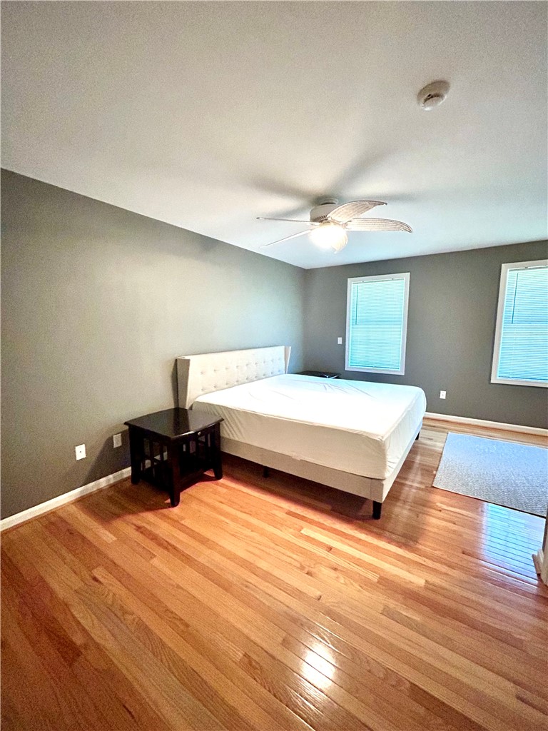 Bedroom with a white upholstered bed, ceiling fan, and polished hardwood floors.