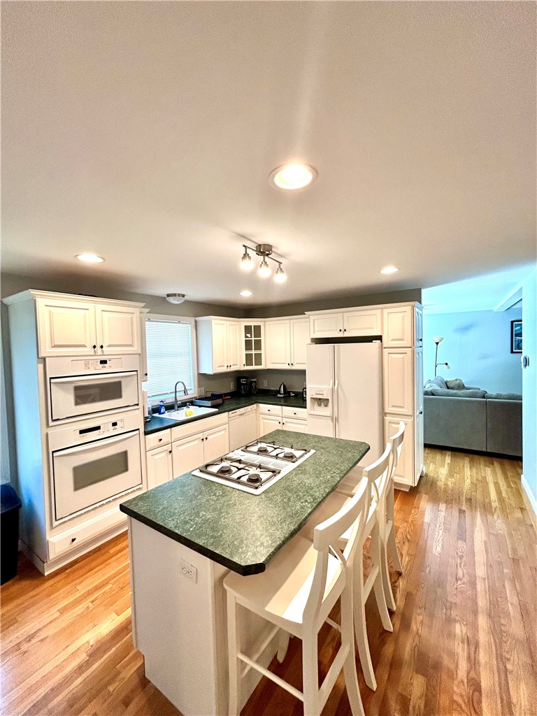 Kitchen with a green stone island cooktop, white cabinetry, double ovens, and hardwood floors.