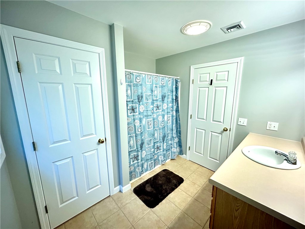 Bathroom with a blue nautical shower curtain, tiled floor, and wood vanity.