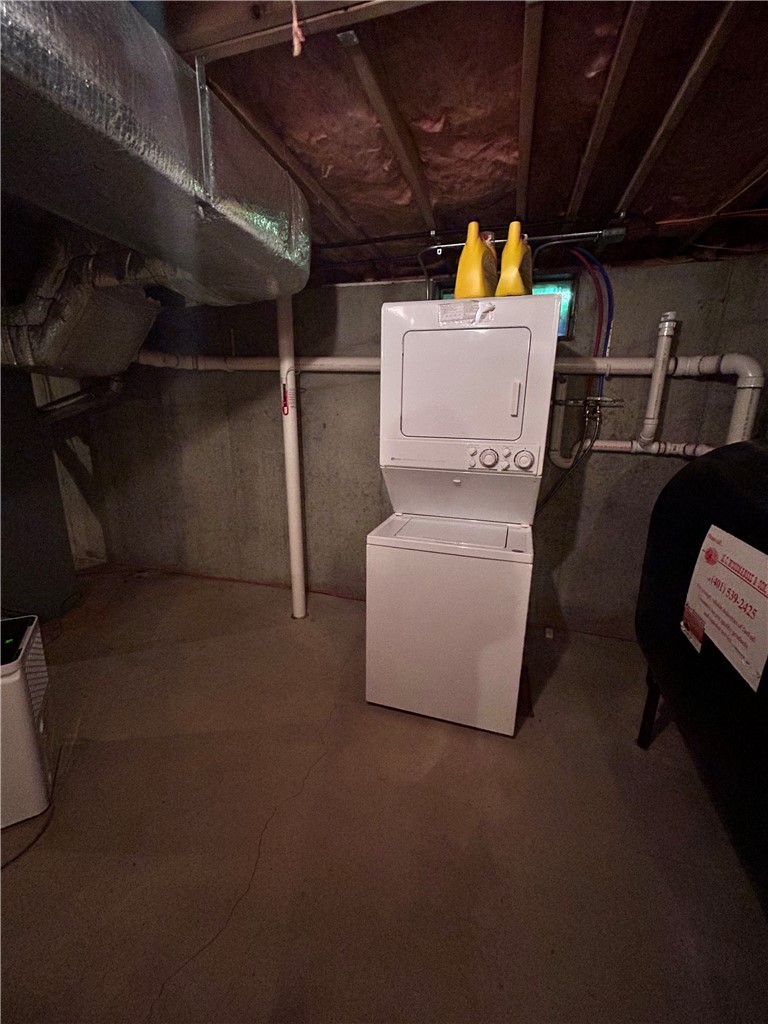 Stacked washer and dryer in an unfinished basement laundry area with exposed pipes and ductwork.