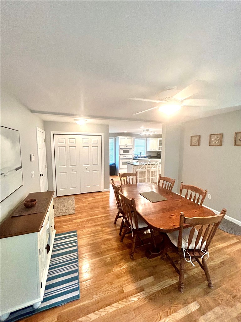 Dining area with a long wooden table and hardwood floors, opening onto a kitchen with a breakfast bar.