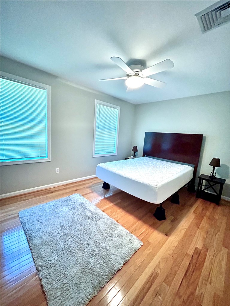 Bedroom with a bed, hardwood floors, two windows, and a ceiling fan.