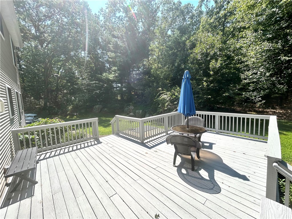 Backyard deck with white railings, patio table and chairs, and a blue umbrella among mature trees.
