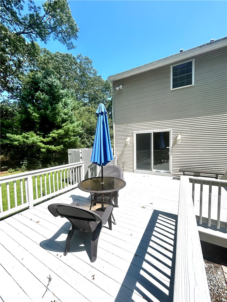 Wooden deck with white railings, outdoor table and chairs, and a closed blue umbrella beside the house.