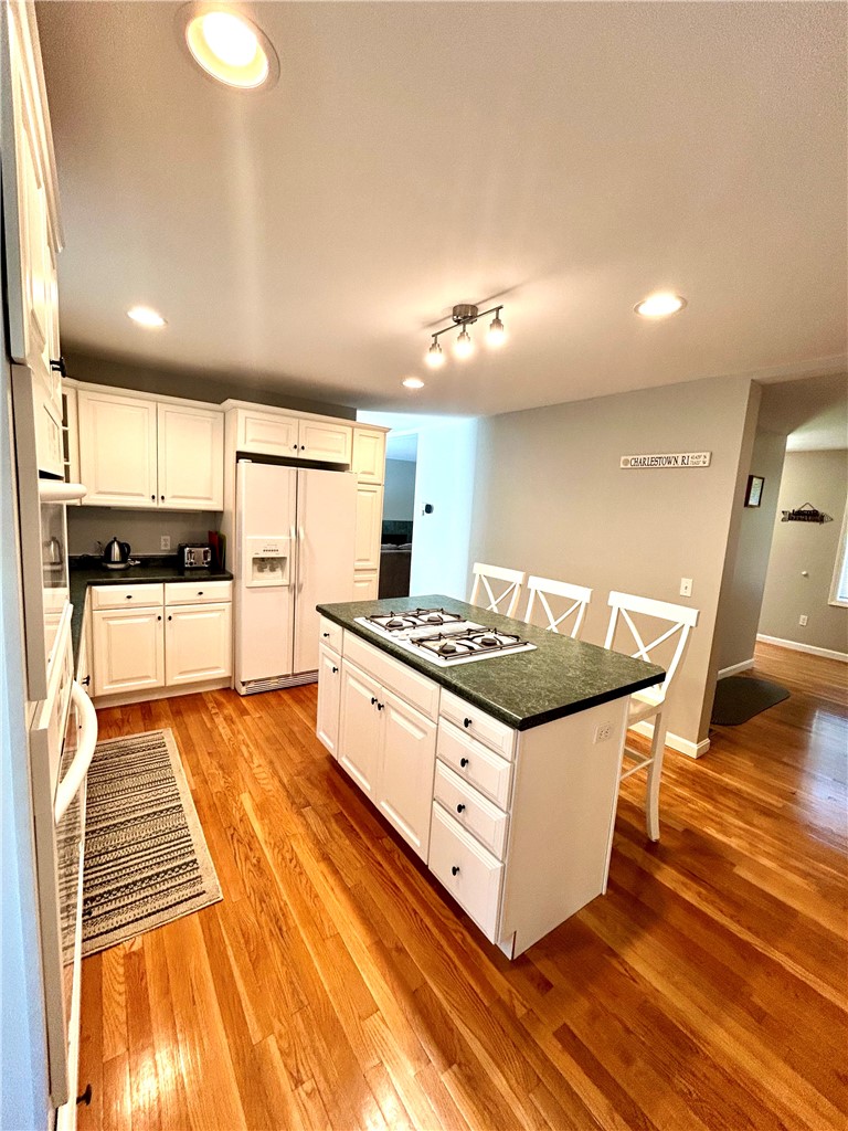 Kitchen with white cabinetry, a dark island cooktop, and glossy hardwood floors.