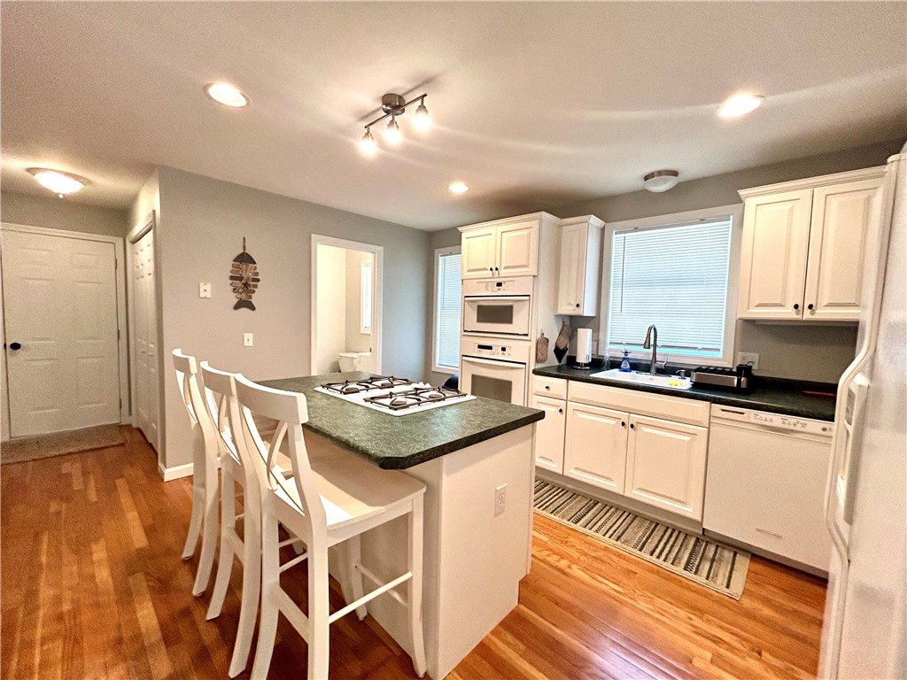 Kitchen with white cabinets, dark countertops, and a cooktop island lined with white bar stools.