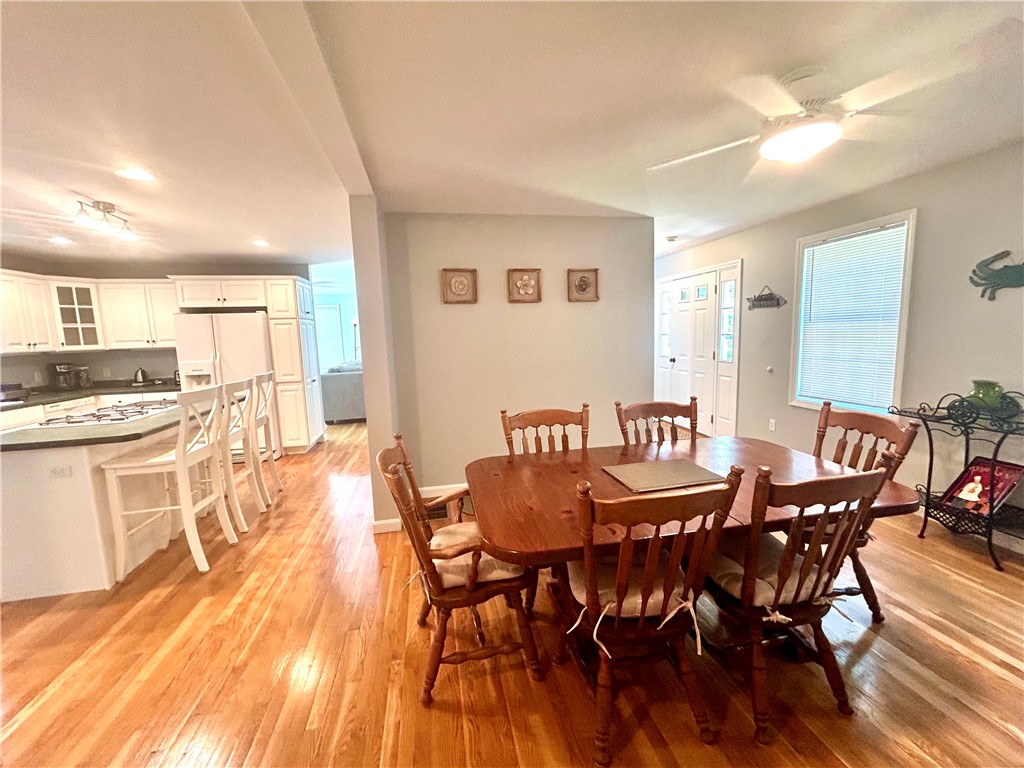 Dining area with a wooden table and chairs, hardwood floors, and an adjoining white kitchen.