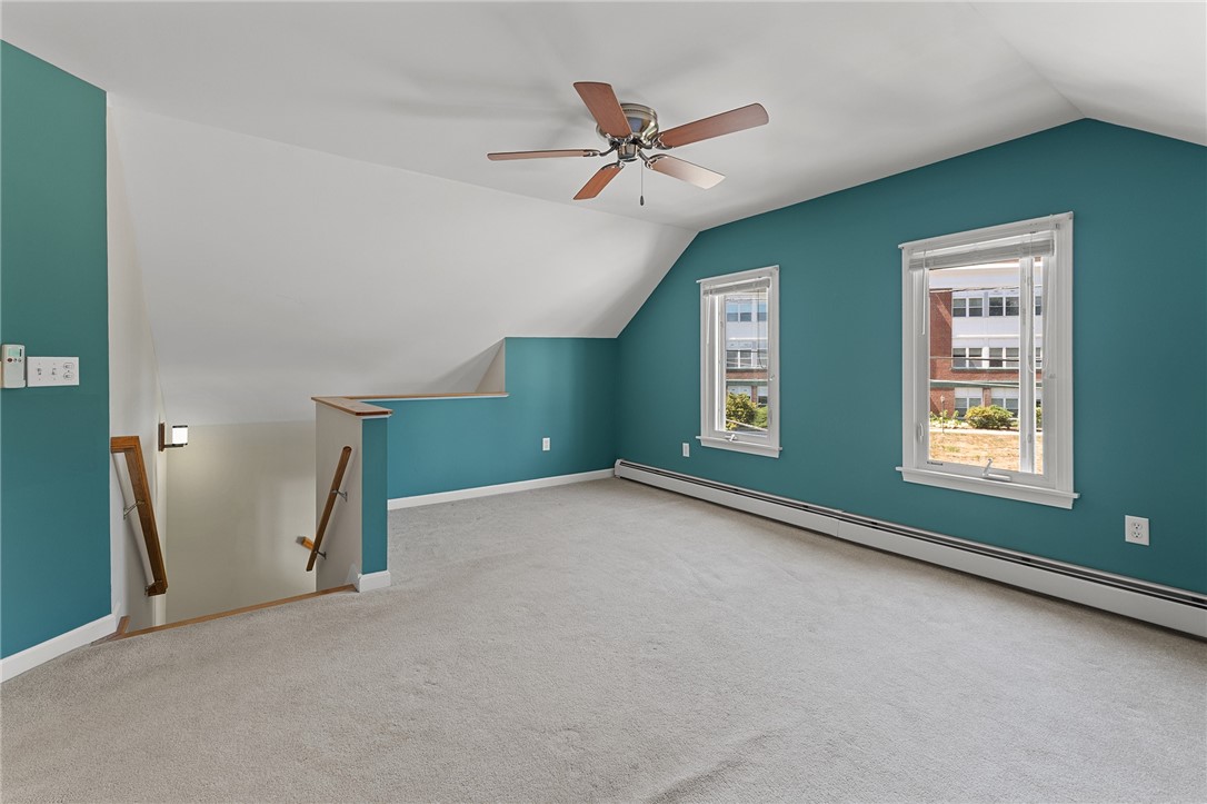 Empty carpeted upper-floor room with teal walls, a sloped ceiling, and two windows.