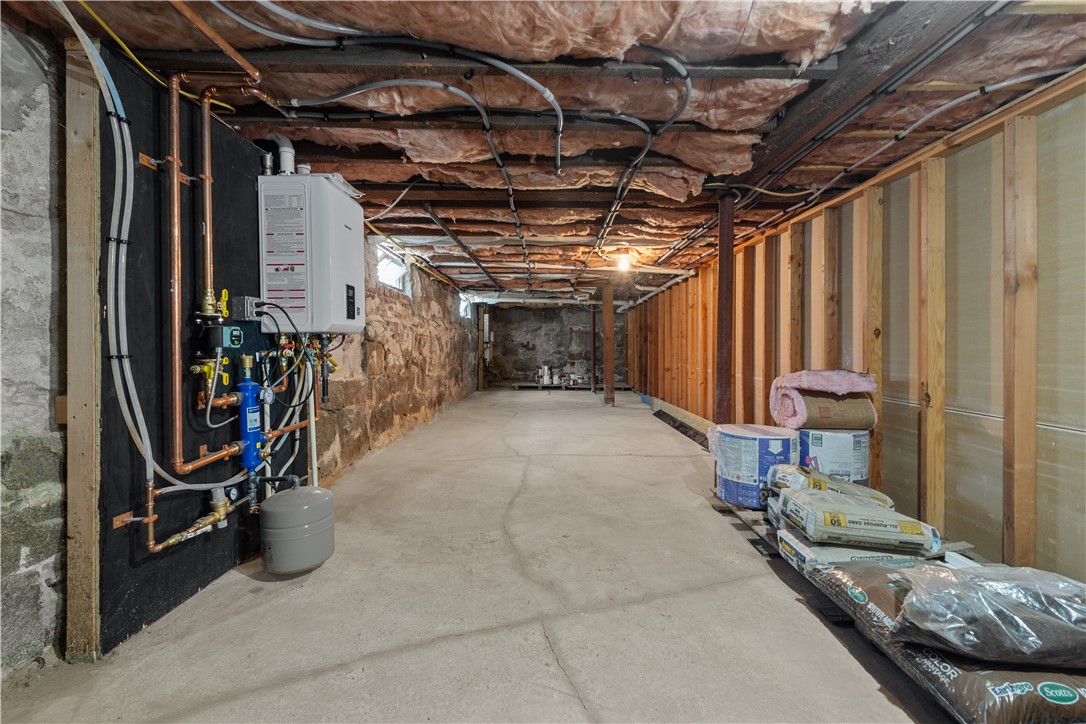 Unfinished basement with exposed framing, stone foundation walls, a concrete floor, and heating equipment.