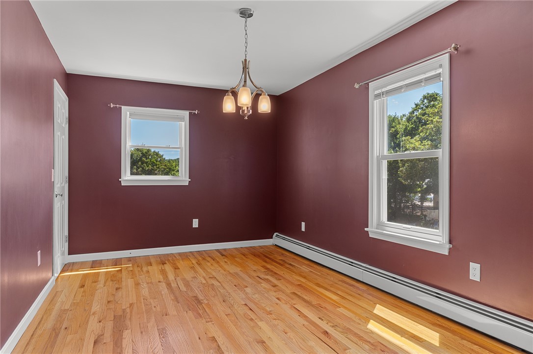 Empty burgundy dining room with hardwood floors, two windows, and a chandelier.