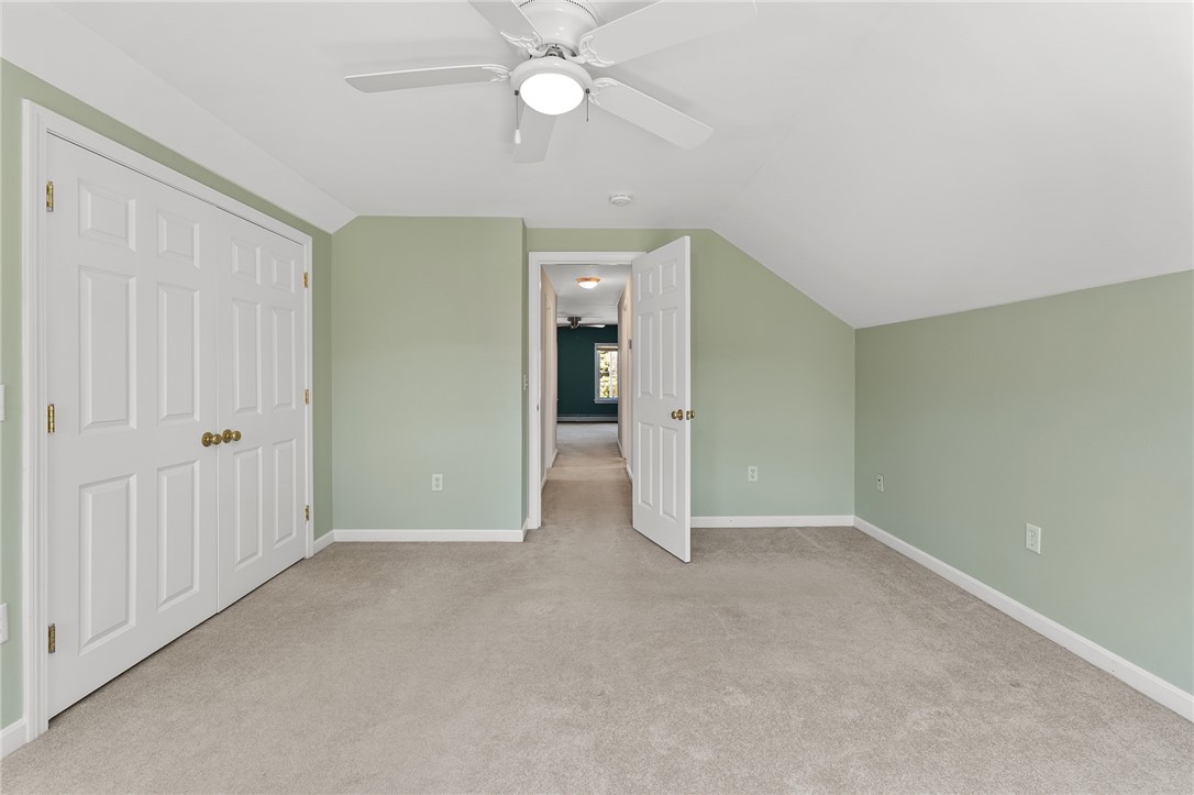 Empty bedroom with pale green walls, beige carpet, ceiling fan, and white closet doors.