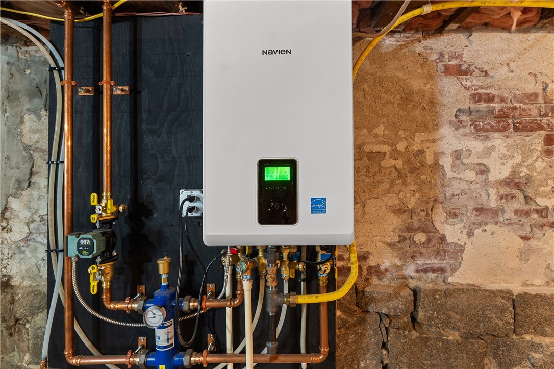 Basement heating unit with copper pipes and valves against an exposed stone and brick wall.