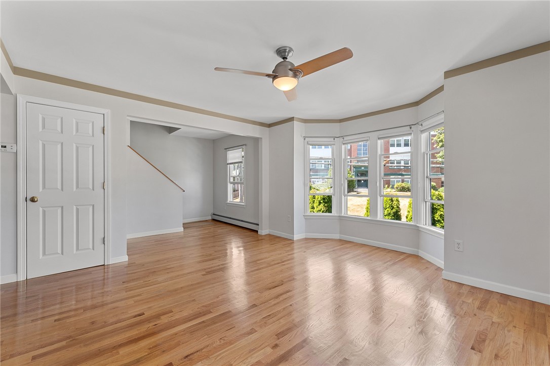 Vacant living room with hardwood floors, bay windows, and a ceiling fan.
