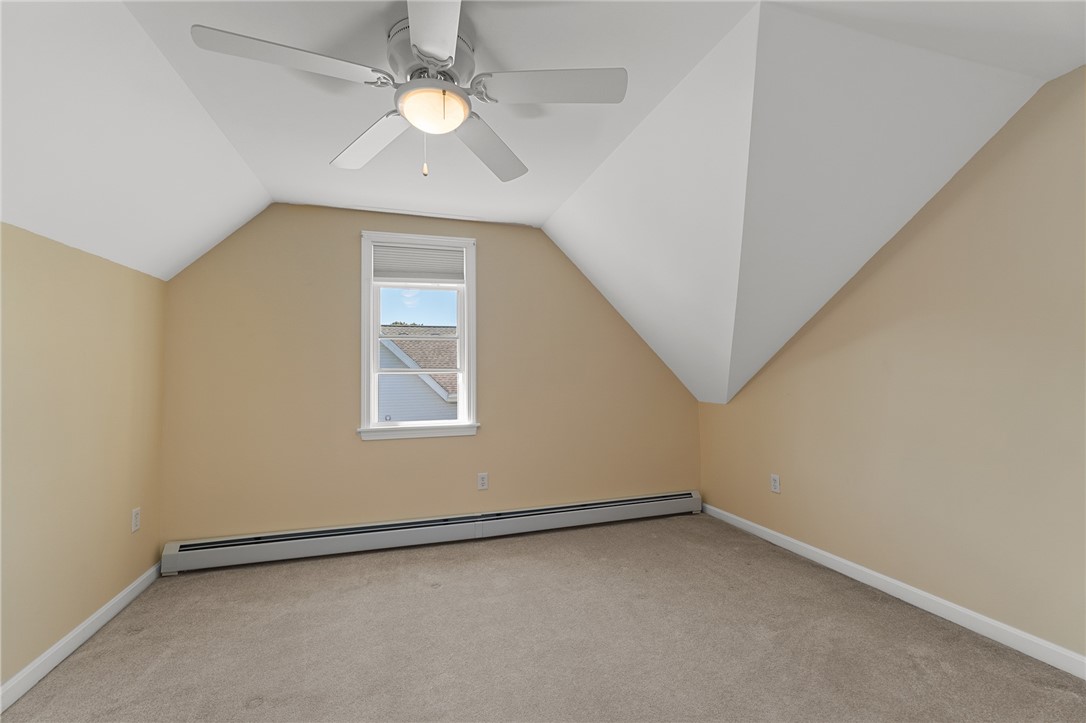 Vacant carpeted bedroom with a sloped ceiling, ceiling fan, and single window.