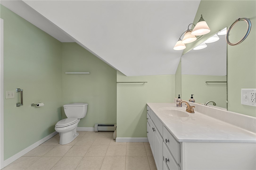 Bathroom with a long white vanity, pale green walls, and a toilet beneath a sloped ceiling.