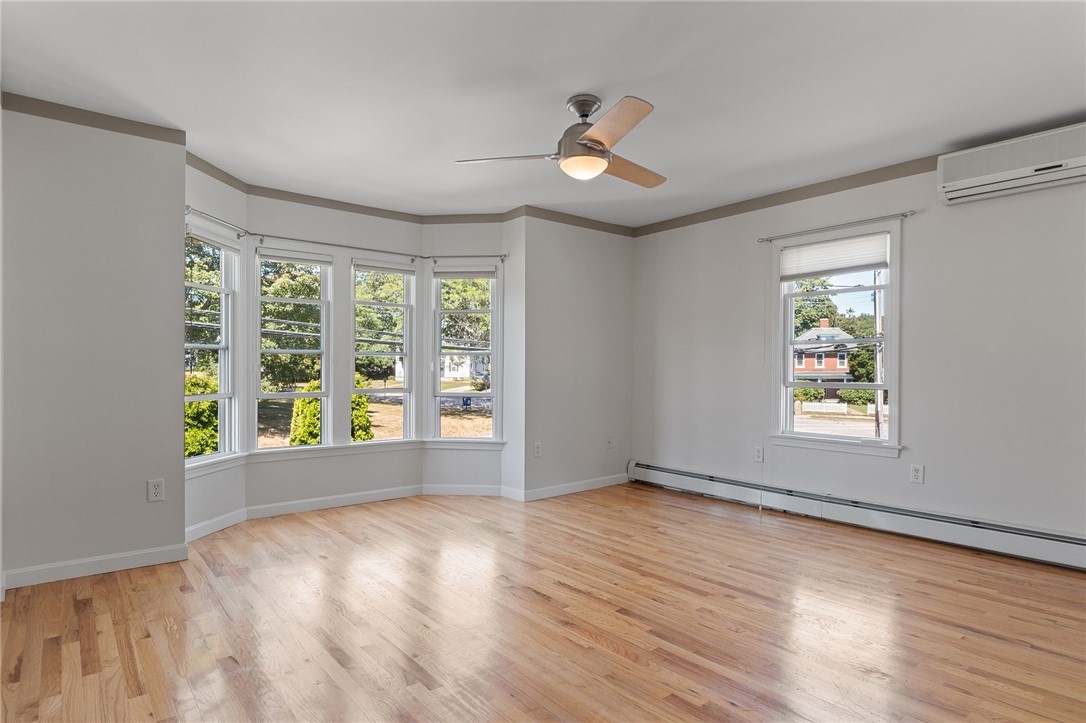 Empty room with hardwood floors, bay windows, ceiling fan, and wall-mounted air conditioner.