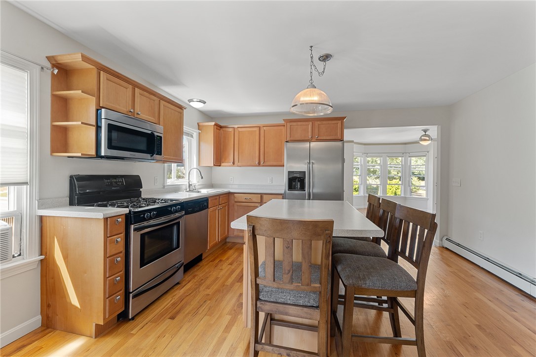 Kitchen with wood cabinets, stainless steel appliances, and a white island beside a windowed dining area.