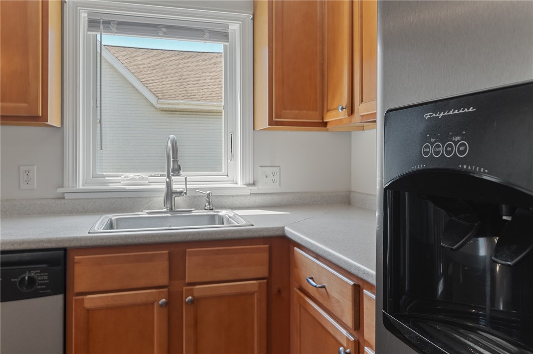 Kitchen with warm wood cabinets, a sink beneath the window, and a black refrigerator with an ice dispenser.