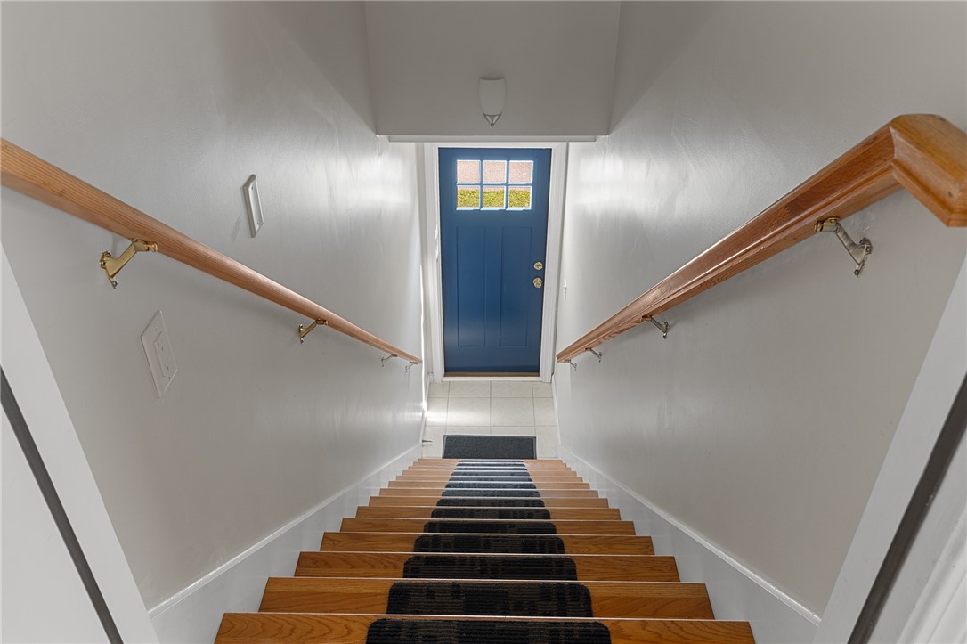 Staircase with polished wood steps and a dark runner leading to a blue door.