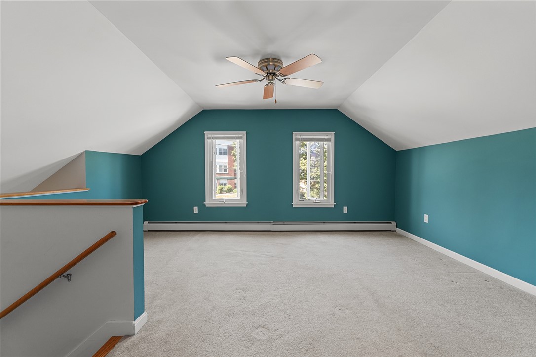 Empty carpeted upper-floor room with teal walls, sloped ceiling, two windows, and ceiling fan.
