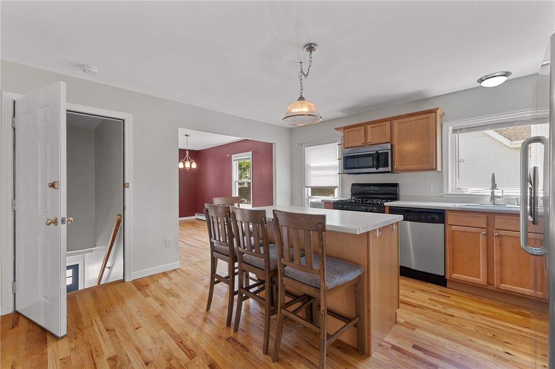 Kitchen with a breakfast island and bar stools, wood cabinets, and hardwood floors.