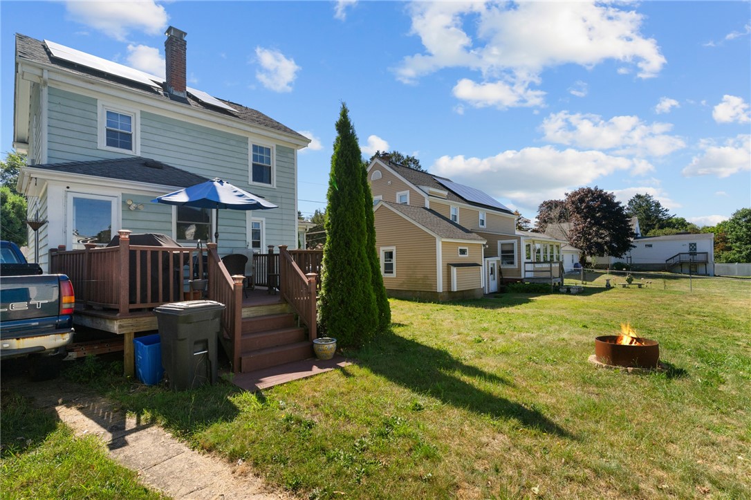 Backyard of a pale blue house with a raised deck, lawn, and fire pit.
