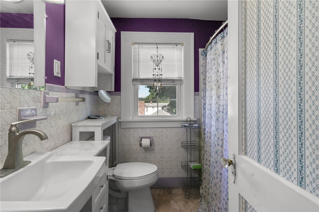 Bathroom with purple walls, patterned tile, white fixtures, and a blue-and-white shower curtain.