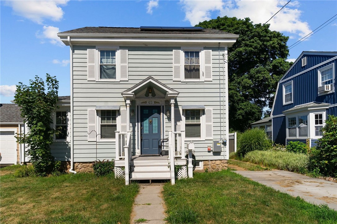Two-story gray house with a blue front door, white shutters, and a small front porch.