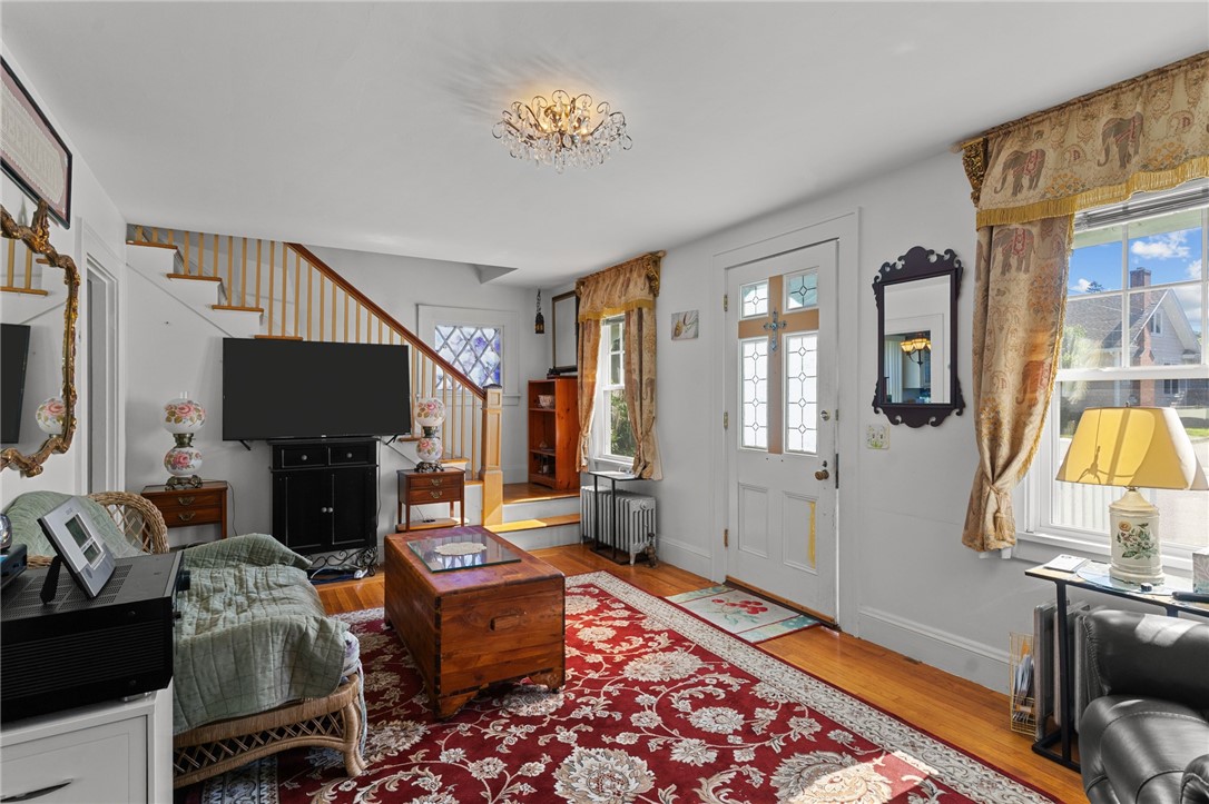 Furnished living room with a red floral rug, hardwood floors, and a staircase.