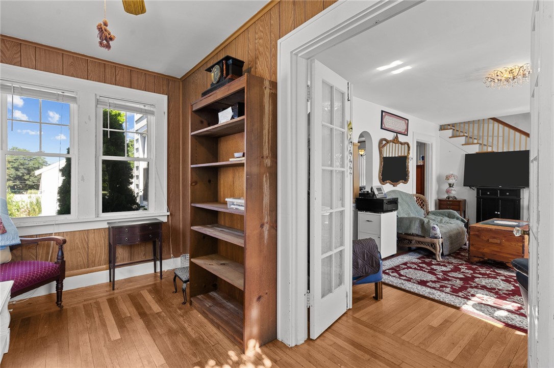 Wood-paneled room with built-in shelves and hardwood floors opening into a living room with a red rug.