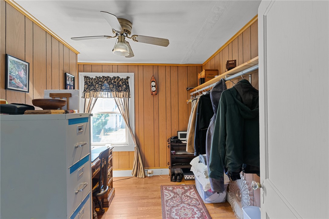 Wood-paneled bedroom with a ceiling fan, clothes rack, and partially visible bed.