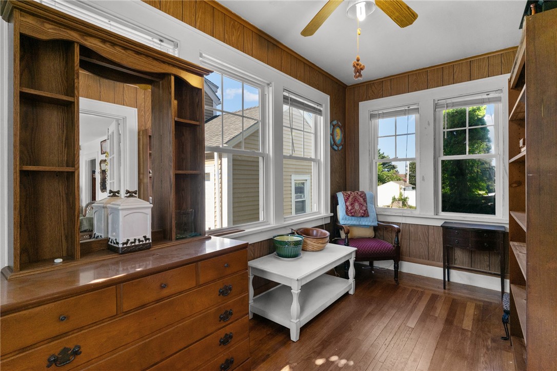 Sitting room with wood-paneled walls, built-in shelves, hardwood floors, and large windows.