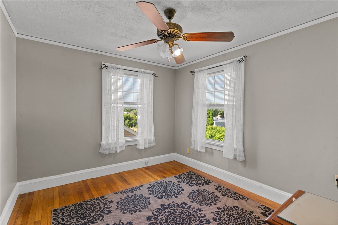 Empty bedroom with lace-curtained windows, hardwood floors, and a ceiling fan.