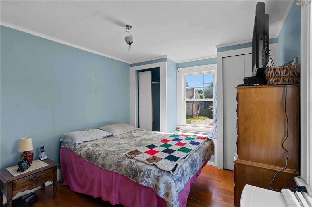 Bedroom with light blue walls, hardwood floors, and a colorful quilt on the bed.