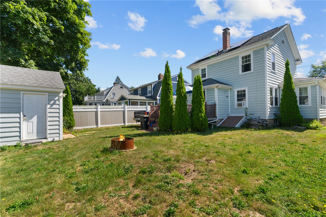 Backyard with a fire pit, detached shed, privacy fence, and light-blue house.