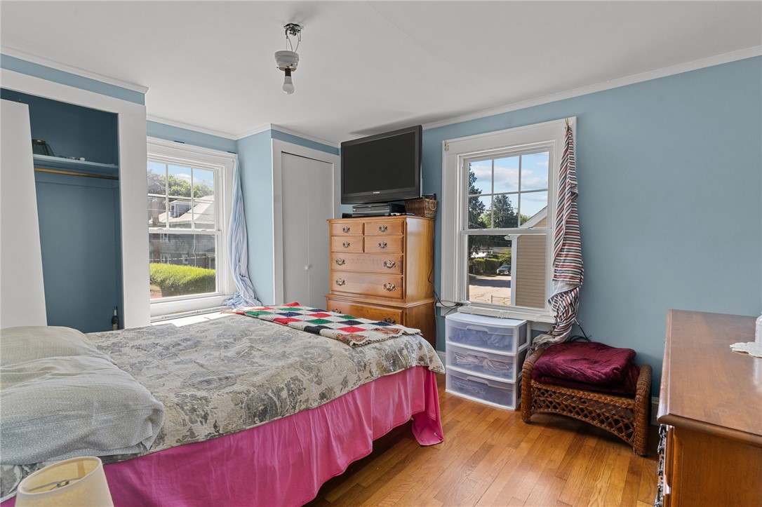 Bedroom with blue walls, hardwood floors, and two windows beside a wooden dresser and television.