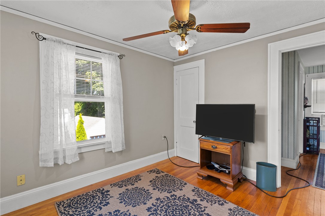Living room with hardwood floors, patterned rug, ceiling fan, and television beside a curtained window.