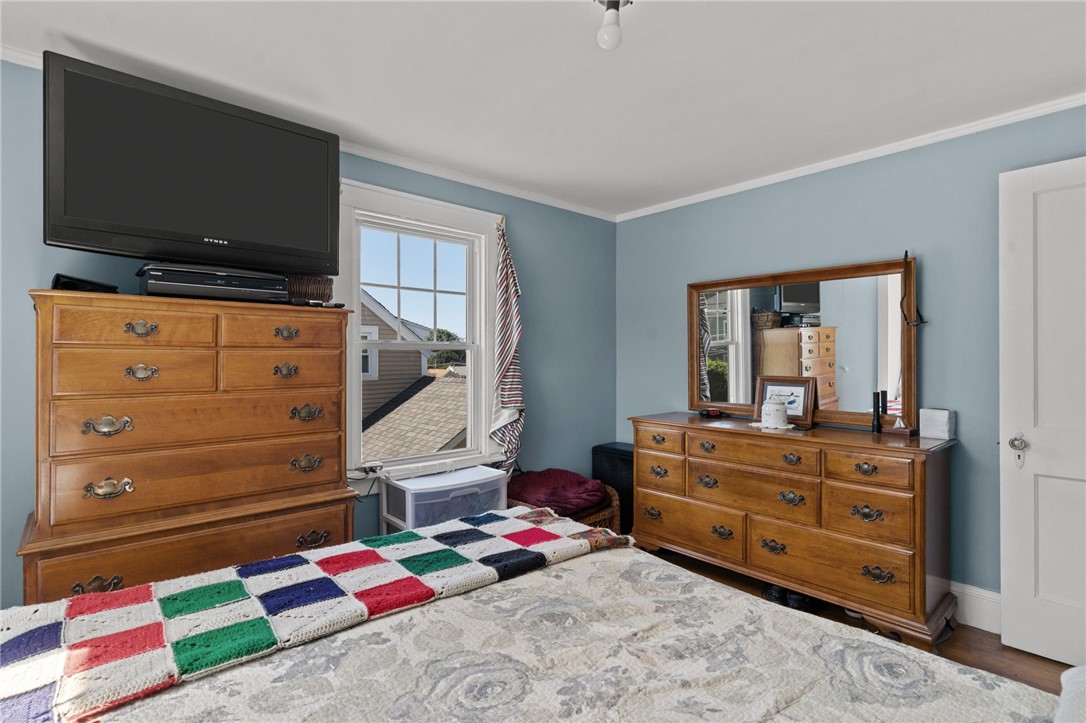 Bedroom with blue walls, wooden dressers, a wall-mounted TV, and a colorful patchwork quilt.