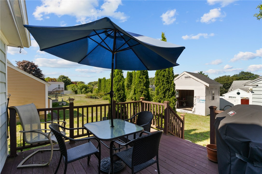 Backyard deck with outdoor dining set beneath a large blue umbrella, overlooking a sunny yard.