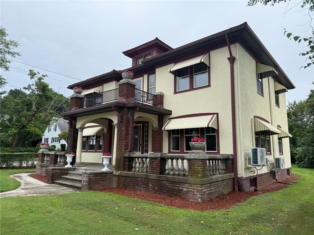 Two-story cream office building with brick porch columns, a balcony, and striped awnings.