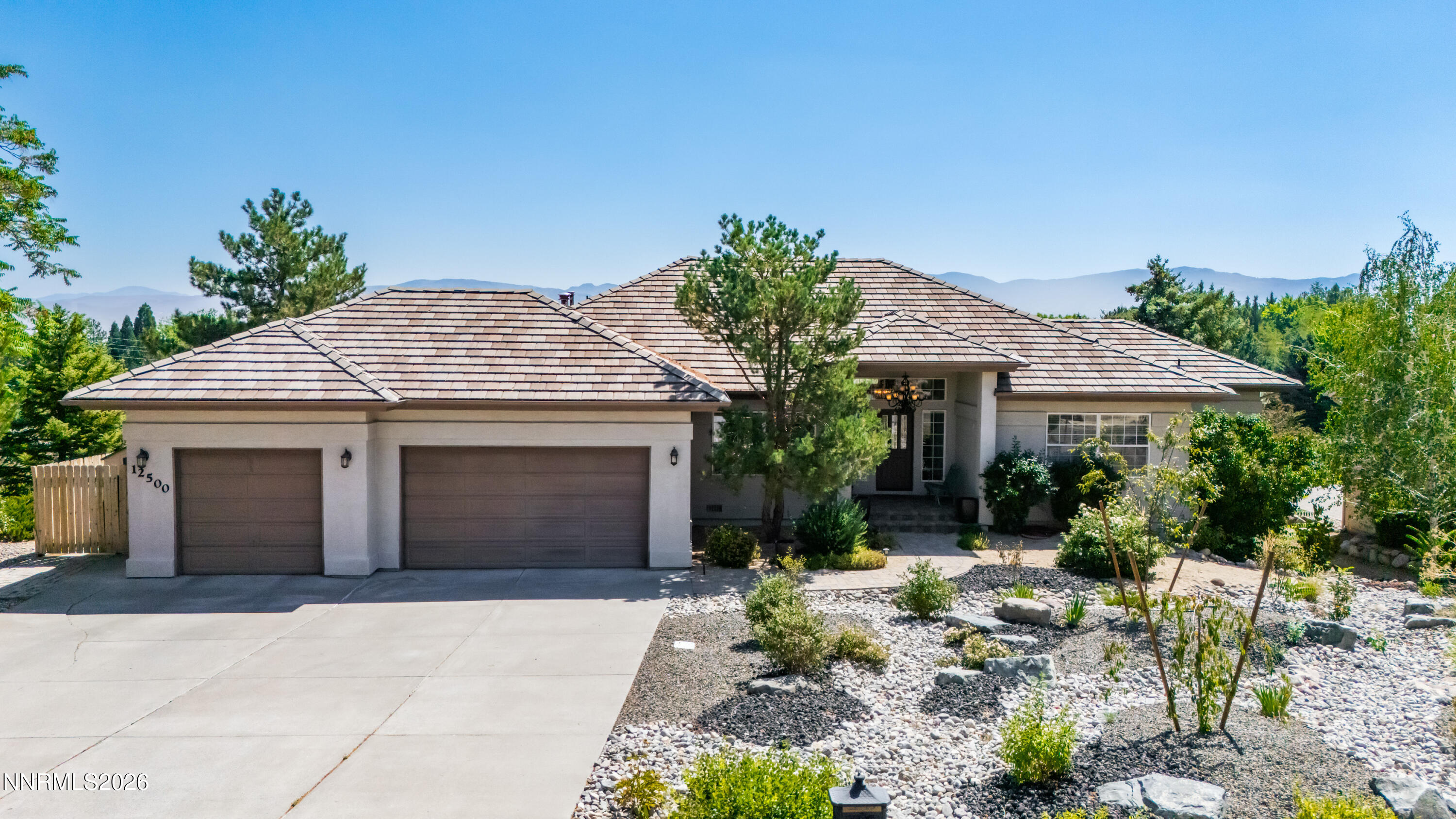 Single-story home with a tile roof and two-car garage, set against a mountain backdrop.