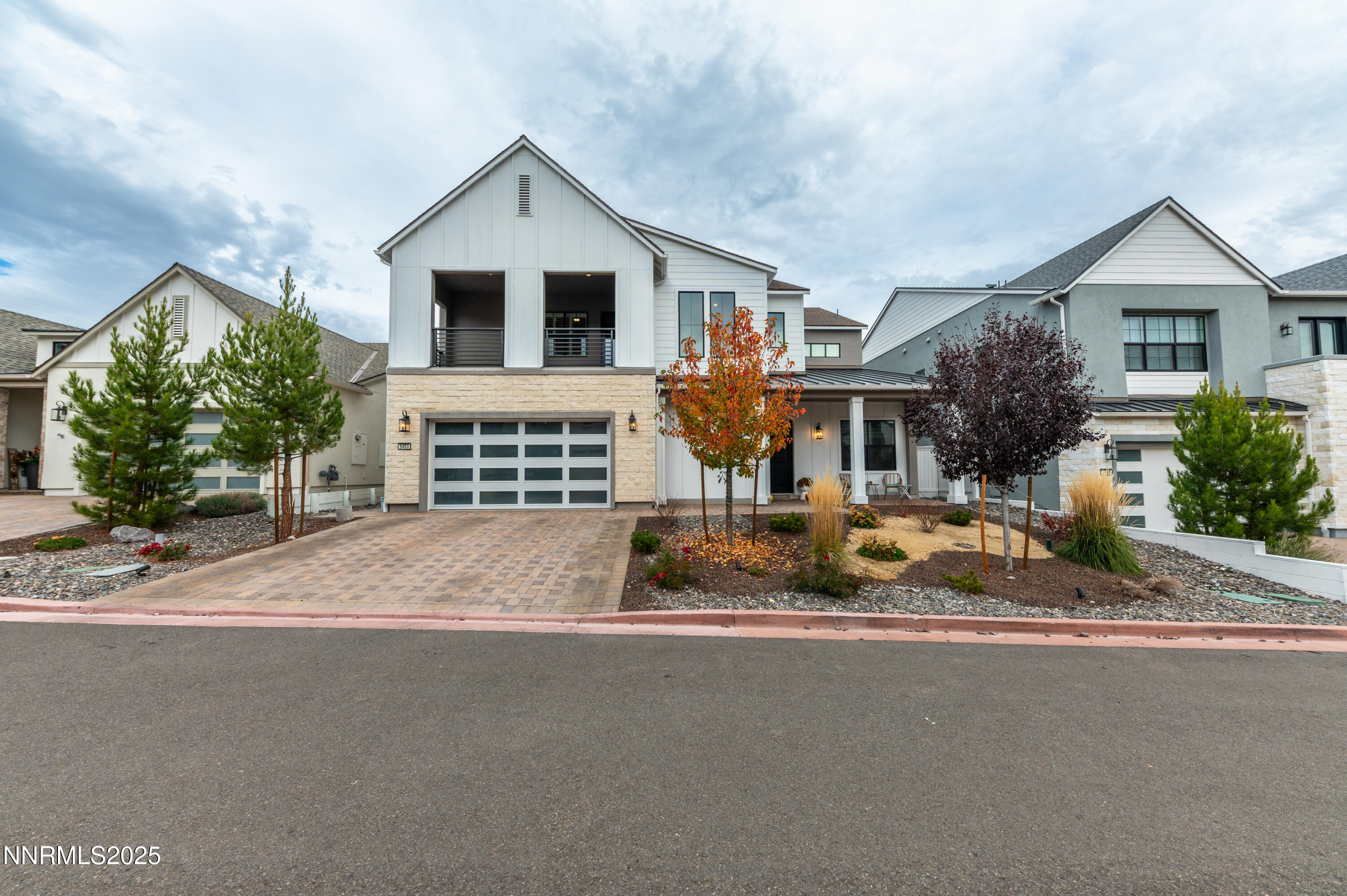 Modern white two-story home with stone facade, double garage, and autumn landscaping.