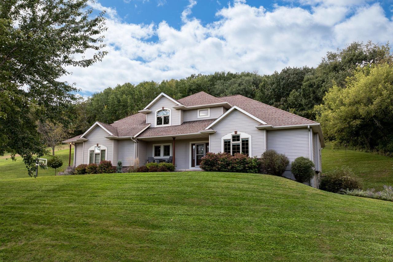 Large gabled home on a sloping lawn, surrounded by mature trees.