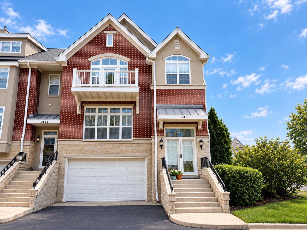 Attached brick townhomes with white balconies, stone stairways, and garage doors.