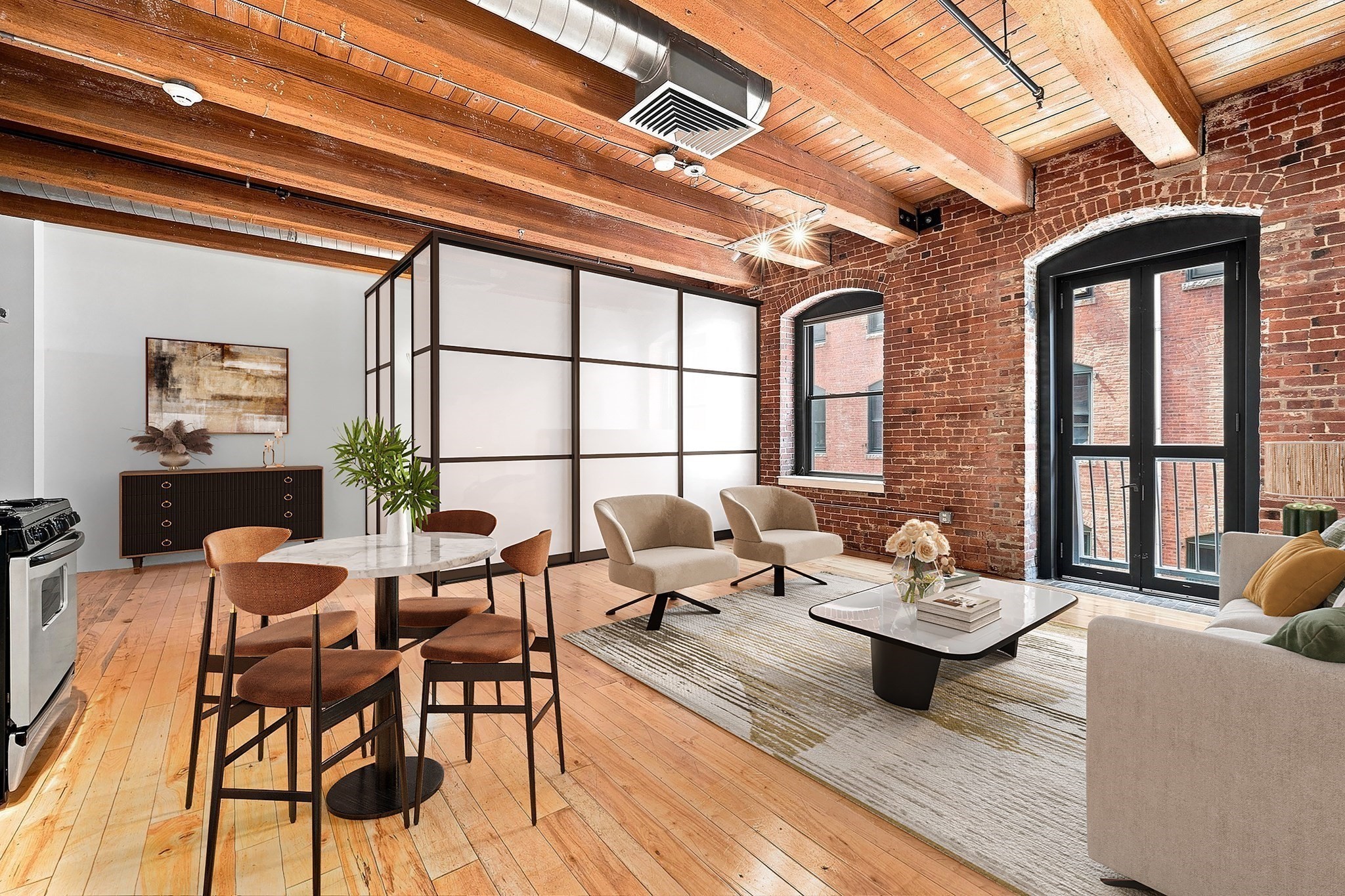 Open-plan loft living and dining area with exposed beams, brick walls, and arched windows.