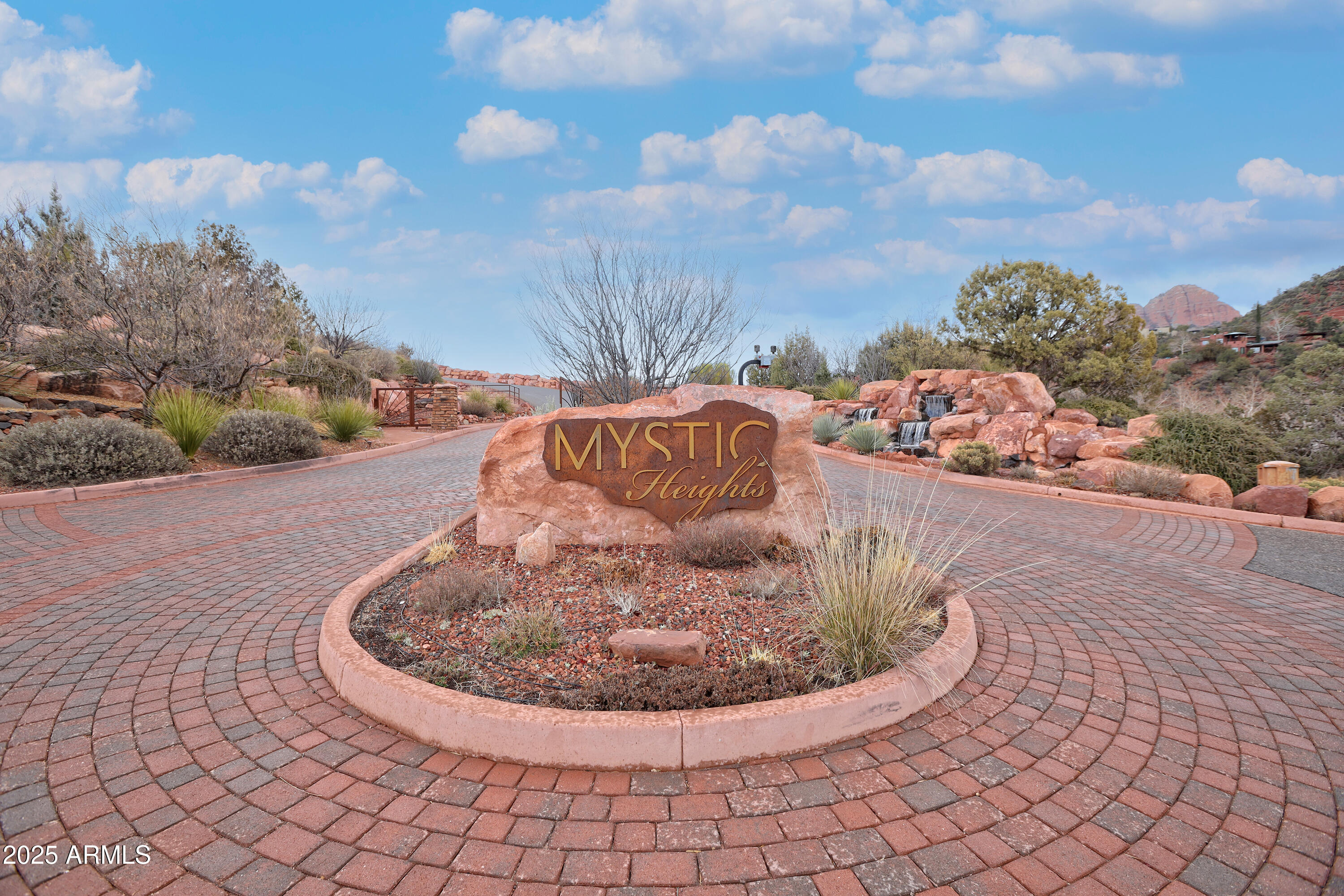 Mystic Heights entrance sign on a red rock amid desert landscaping and a circular brick drive.