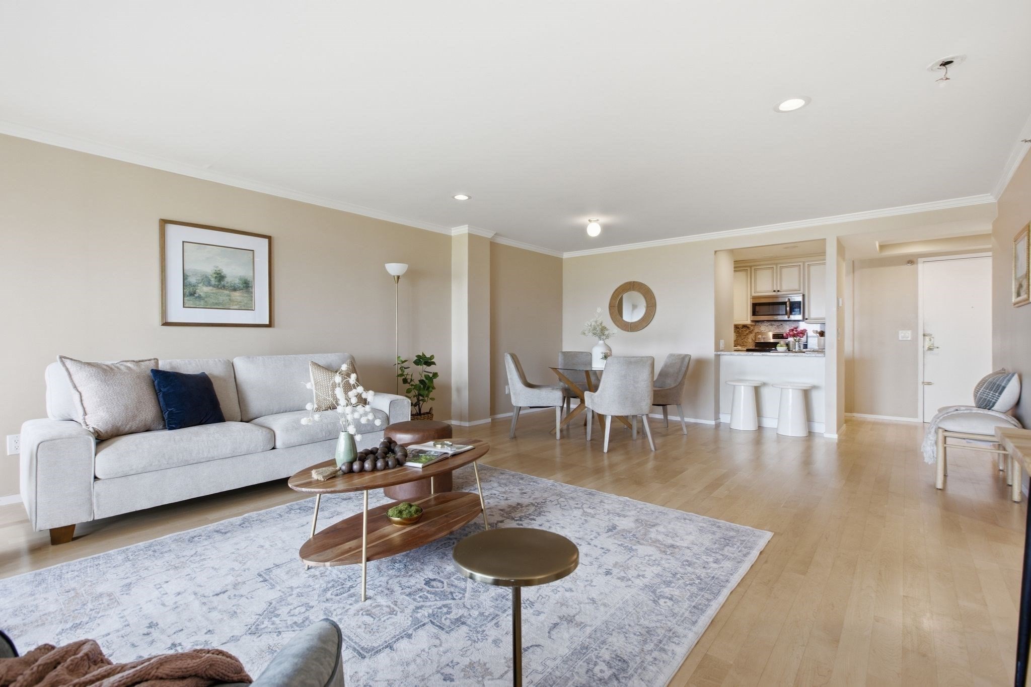 Open-plan living and dining room with a gray sofa, patterned rug, and kitchen pass-through.