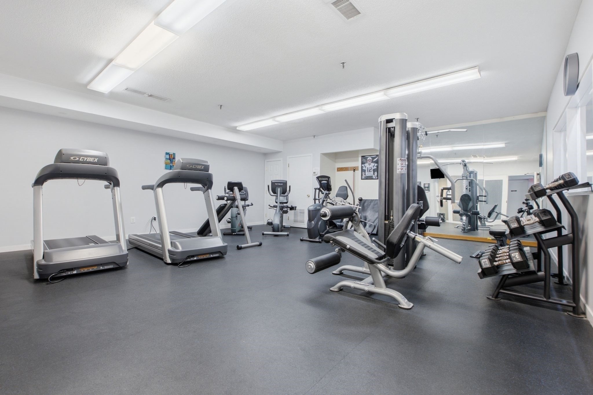 Fitness room with treadmills, weight machines, and a dumbbell rack beside a mirrored wall.