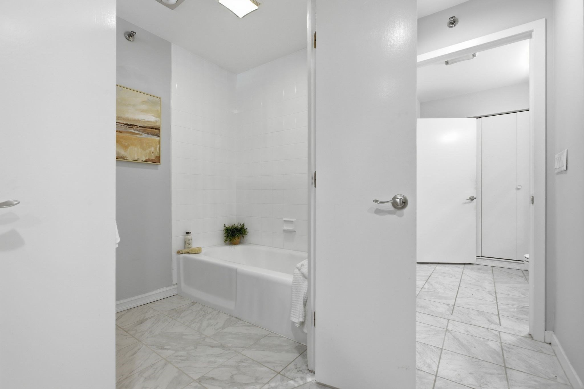 Bathroom with a white bathtub, tiled walls, and marble-look flooring.