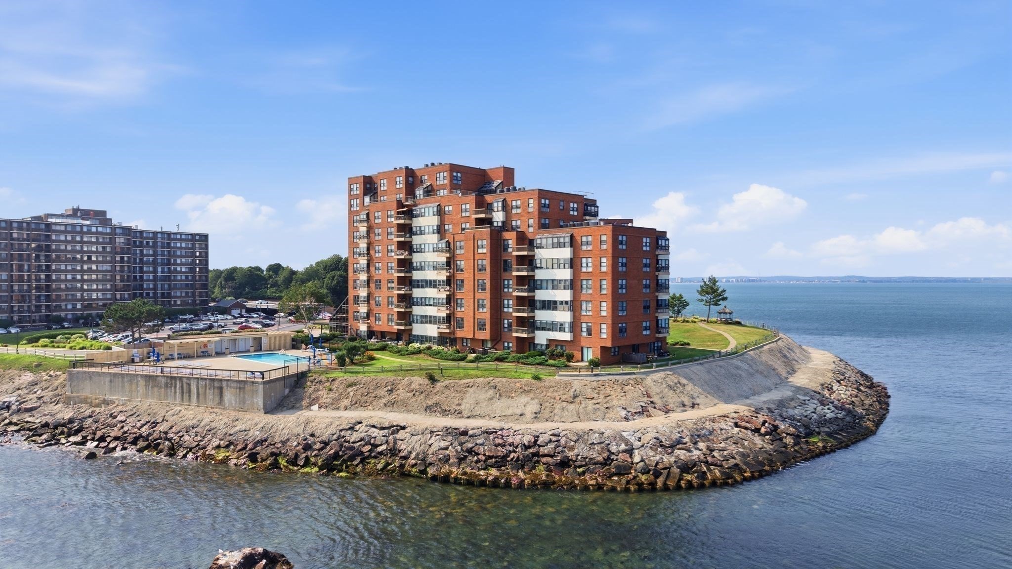 Waterfront condominium buildings on a rocky point, with a pool and open water.